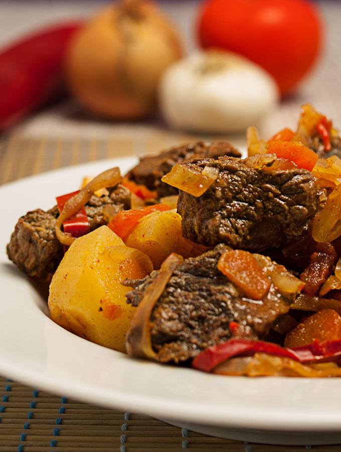 Bosanski Lonac, ein reichhaltiger Fleischeintopf aus Bosnien, mit Rindfleisch, Zwiebeln, Paprika und Lorbeerblatt in tiefem weißen Teller.