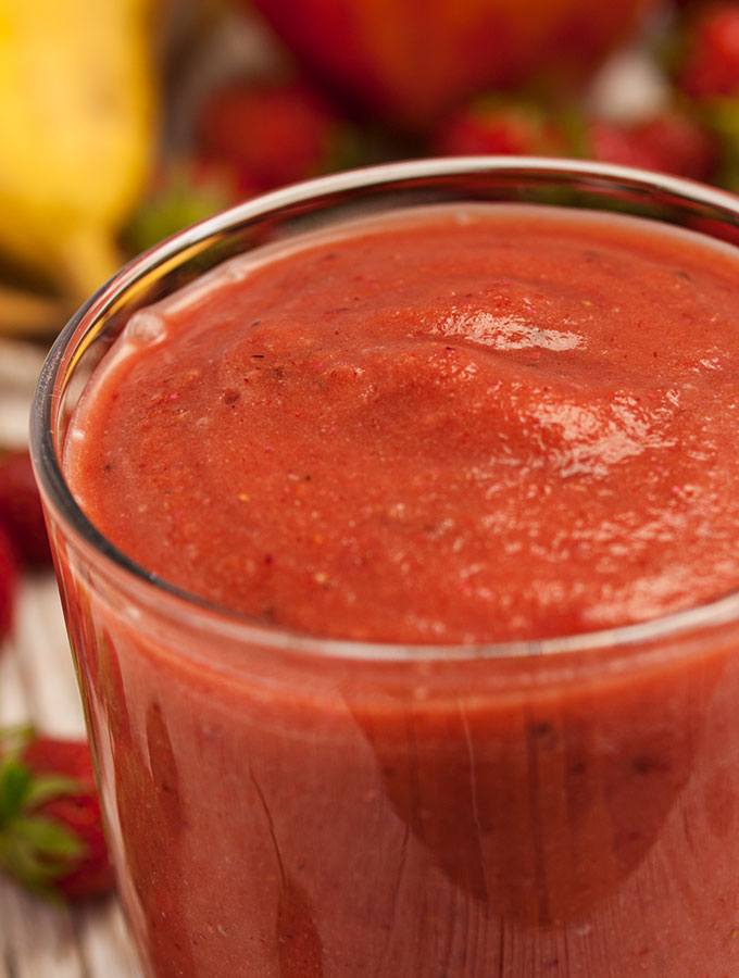 Erdbeer-Power-Smoothie im Glas, fotografiert als Nahaufnahme. Als Dekorationen dienen Erdbeeren und Bananen.