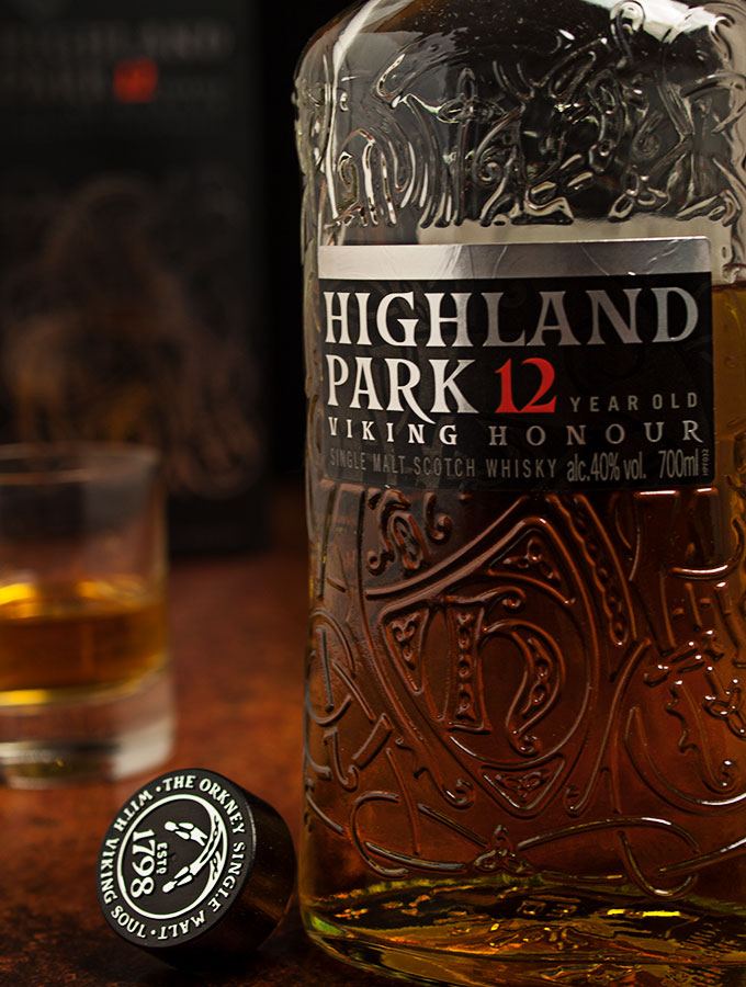 Nahaufnahme einer Flasche Highland Park Single Malt Scotch Whisky Viking Honour 12 Jahre mit Korken danebenliegend. im Hintergrund ein Glas Highland Park Single Malt Scotch Whisky Viking Honour 12 Jahre sowie die Geschenkverpackung.